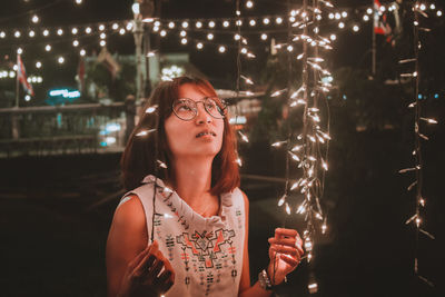 Portrait of woman standing by illuminated lights at night