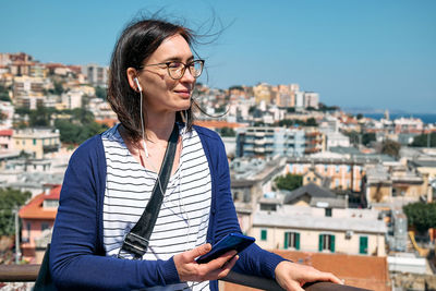 Happy smiling woman listening music, song or audio guide at mobile phone while enjoying a view 