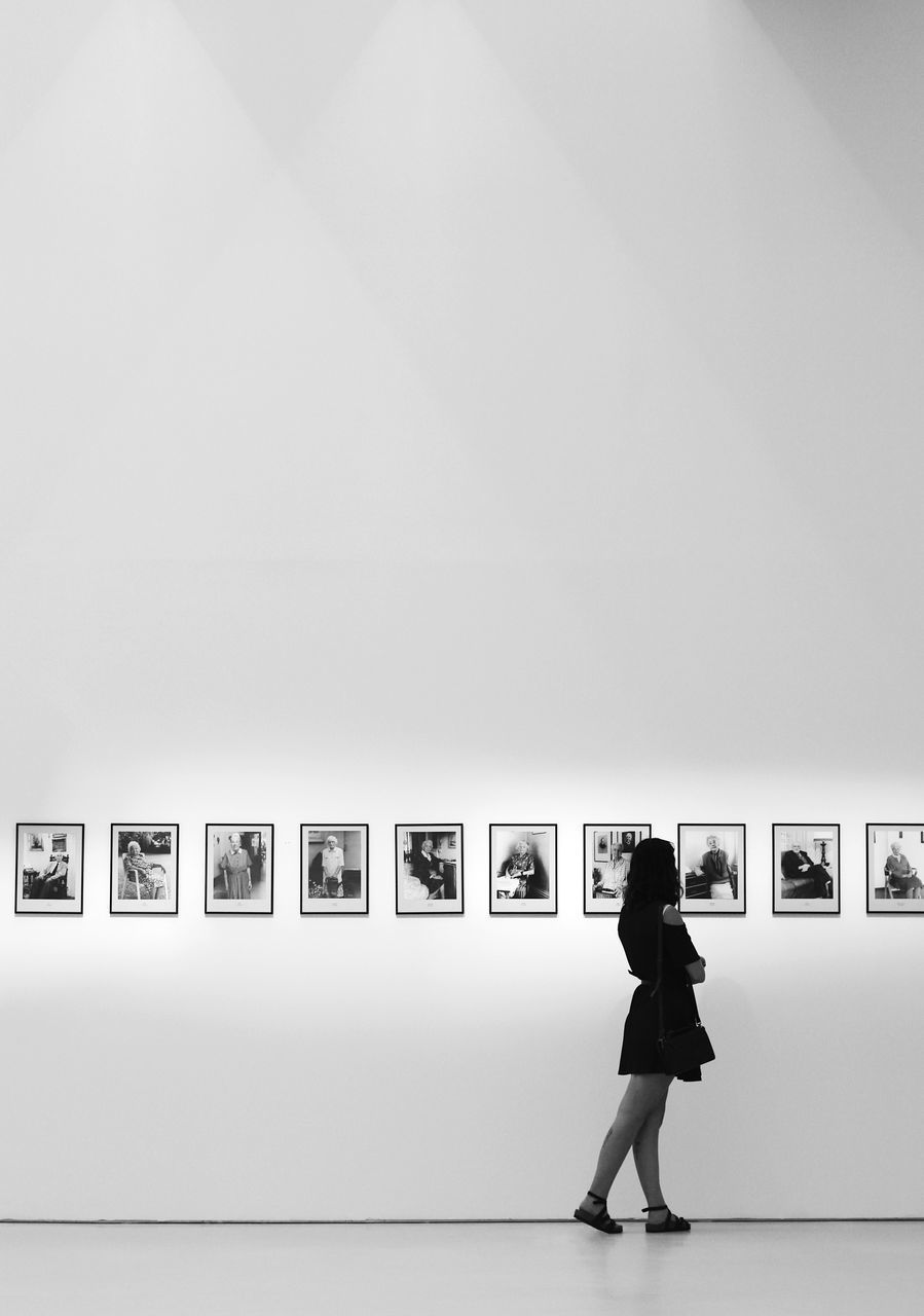 SIDE VIEW OF WOMAN STANDING AGAINST WALL