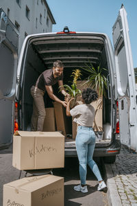 Multiracial couple helping each other while unloading plants from van trunk