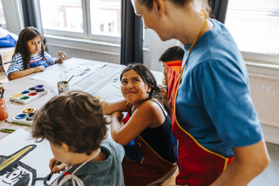 High angle view of smiling girl talking with female professor dusting art class in school