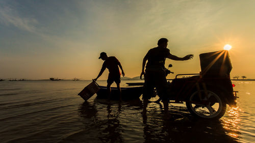 Silhouette men working in sea against sky during sunset