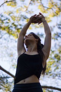  woman with arms raised standing against tree