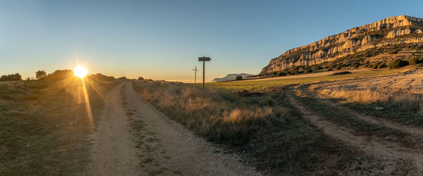 Dirt road amidst landscape against sky during sunset