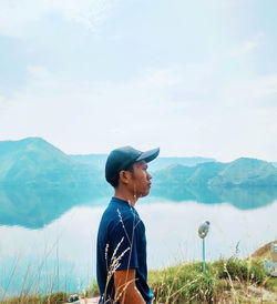 Side view of man standing by lake against mountains and sky