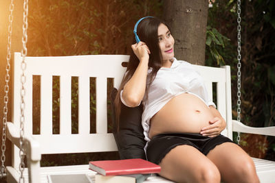 Pregnant woman listening music while sitting on swing at yard