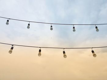 Low angle view of light bulbs hanging against sky