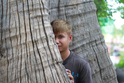 Portrait of boy peeking from tree trunk