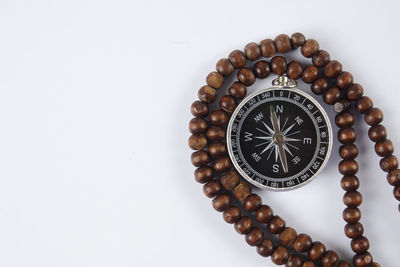 Close-up of compass with bead necklace over white background