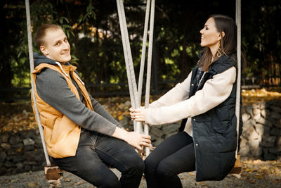 Smiling man with girlfriend sitting on swing