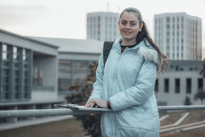 Portrait of young woman holding clipboard outdoors