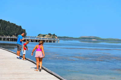 Rear view of women walking on beach against clear blue sky