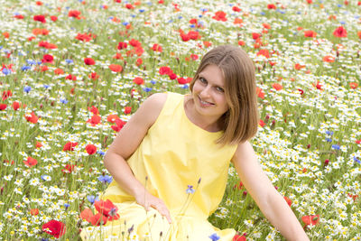 A beautiful young blonde woman in a yellow dress stands among a flowering field