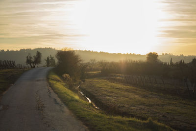 Road amidst field against sky during sunset