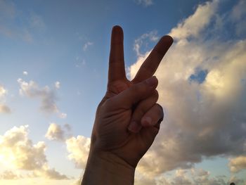 Low angle view of person hand gesturing peace sign against sky