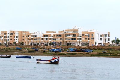 Boats moored in canal by buildings against clear sky