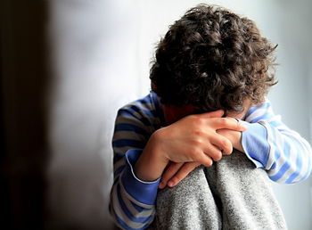 Boy praying with hands over face against wall at home stock photo