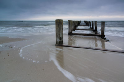 Wooden posts on beach against sky