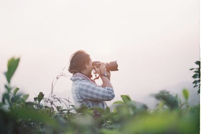 Side view of man photographing against sky