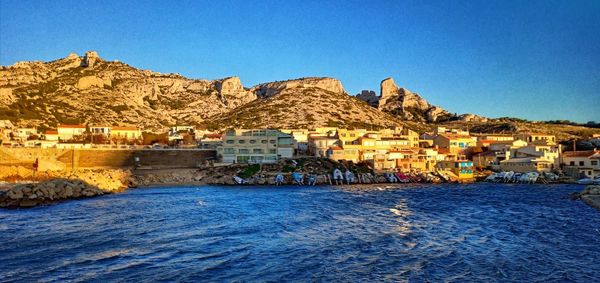 Buildings by sea against clear blue sky