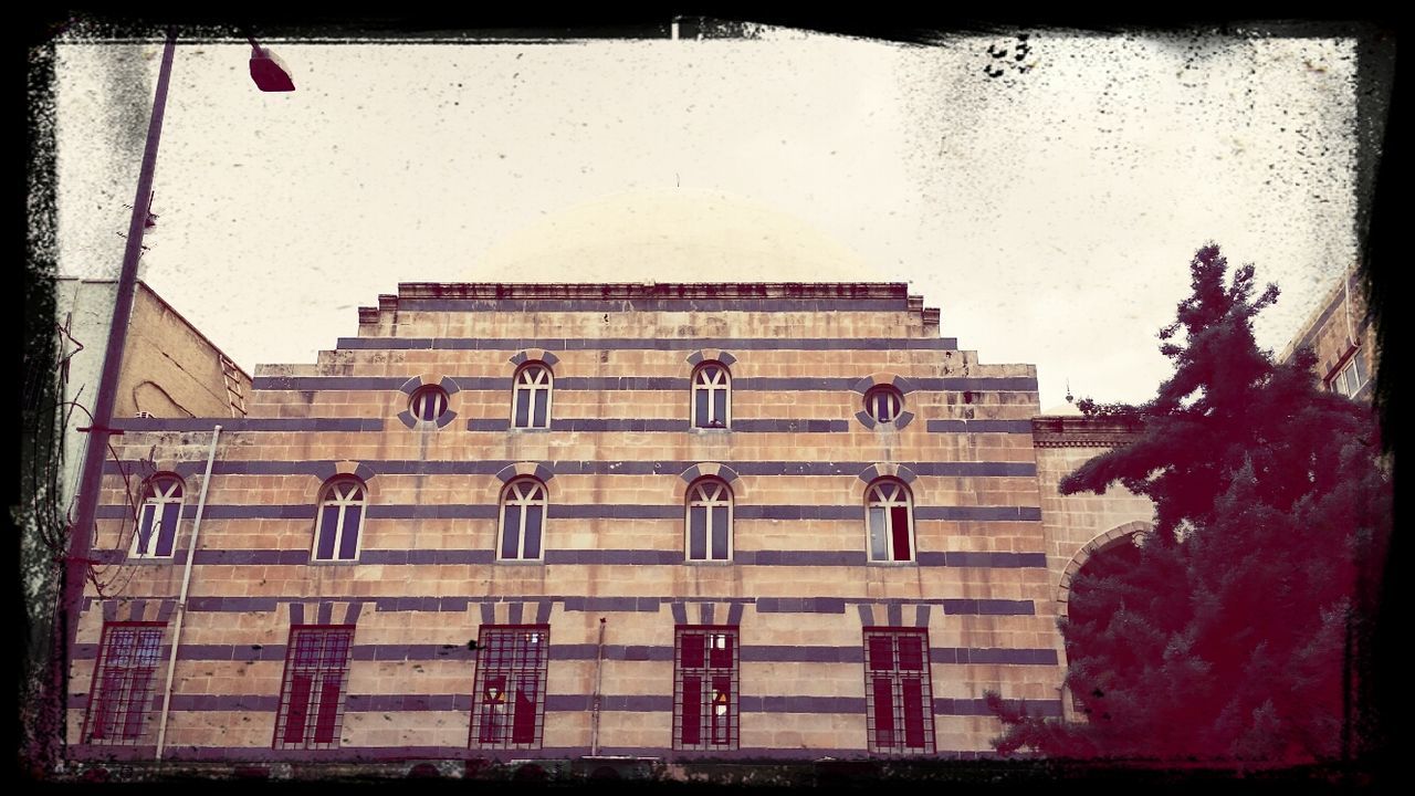 building exterior, architecture, built structure, low angle view, transfer print, auto post production filter, window, building, day, facade, city, art and craft, outdoors, art, no people, sky, flag, creativity, wall - building feature, red