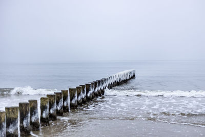 Wooden posts in sea against clear sky