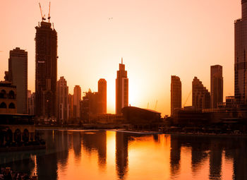 Buildings by river against sky during sunset