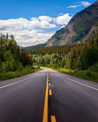 Empty road along trees and mountains against sky