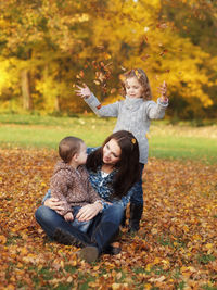 Mother with children sitting on leaves at park during autumn