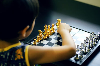 Rear view of boy playing chess at table