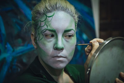 Close-up of young woman applying make-up in room