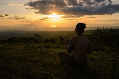 Man photographing while sitting on field against sky during sunset