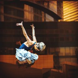 Full length of young woman jumping against buildings