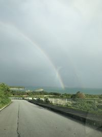 Rainbow over road against sky during rainy season