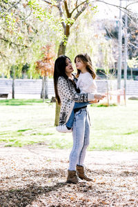 Side view of mother carrying cute daughter while standing in park