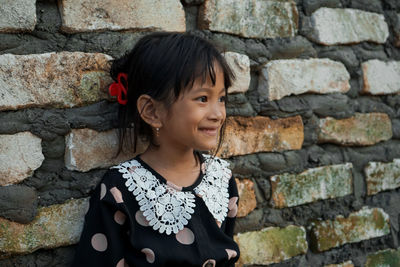 Smiling girl standing by stone wall