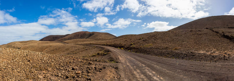 Dirt road amidst desert against sky