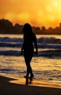 Rear view of woman standing at beach during sunset