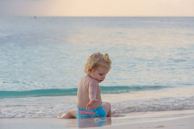 Shirtless boy sitting on shore at beach