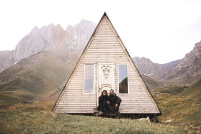 Couple sitting in front of log cabin in kazbegi national park