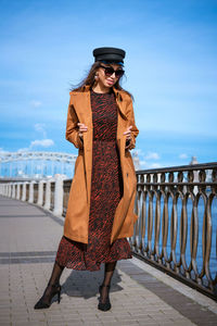 Beautiful woman in a cap and jacket posing while standing on the embankment