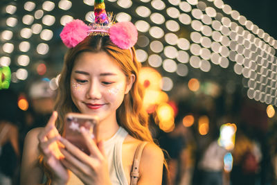 Young woman using mobile against illuminated lights