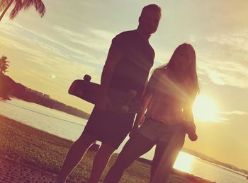 Couple standing by sea against sky during sunset