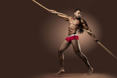 Full length of athlete exercising with rope against brown background