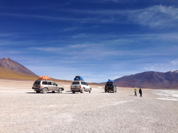 People by vehicles on desert against sky