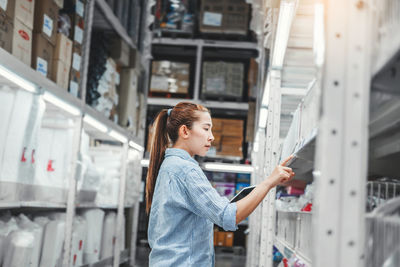 Side view of woman holding digital tablet while standing in warehouse