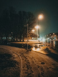 Empty road by illuminated city against sky at night