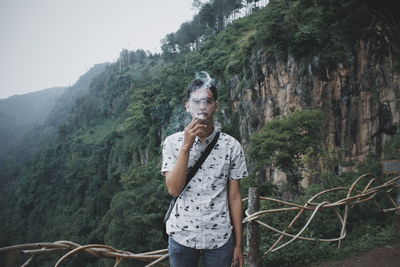 Portrait of man smoking while standing on mountain against sky