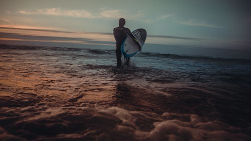 Man standing on beach against sky during sunset