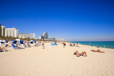 People at beach against clear blue sky